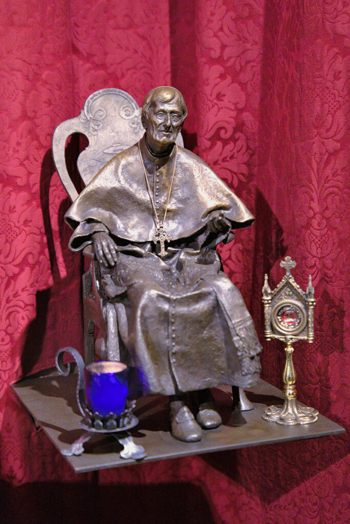 Brozestatue von Kardinal Newman auf seinem Lehrstuhl mit seinem Wappen. Er wird von Benedikt XVI als Kirchenlehrer angesehen.